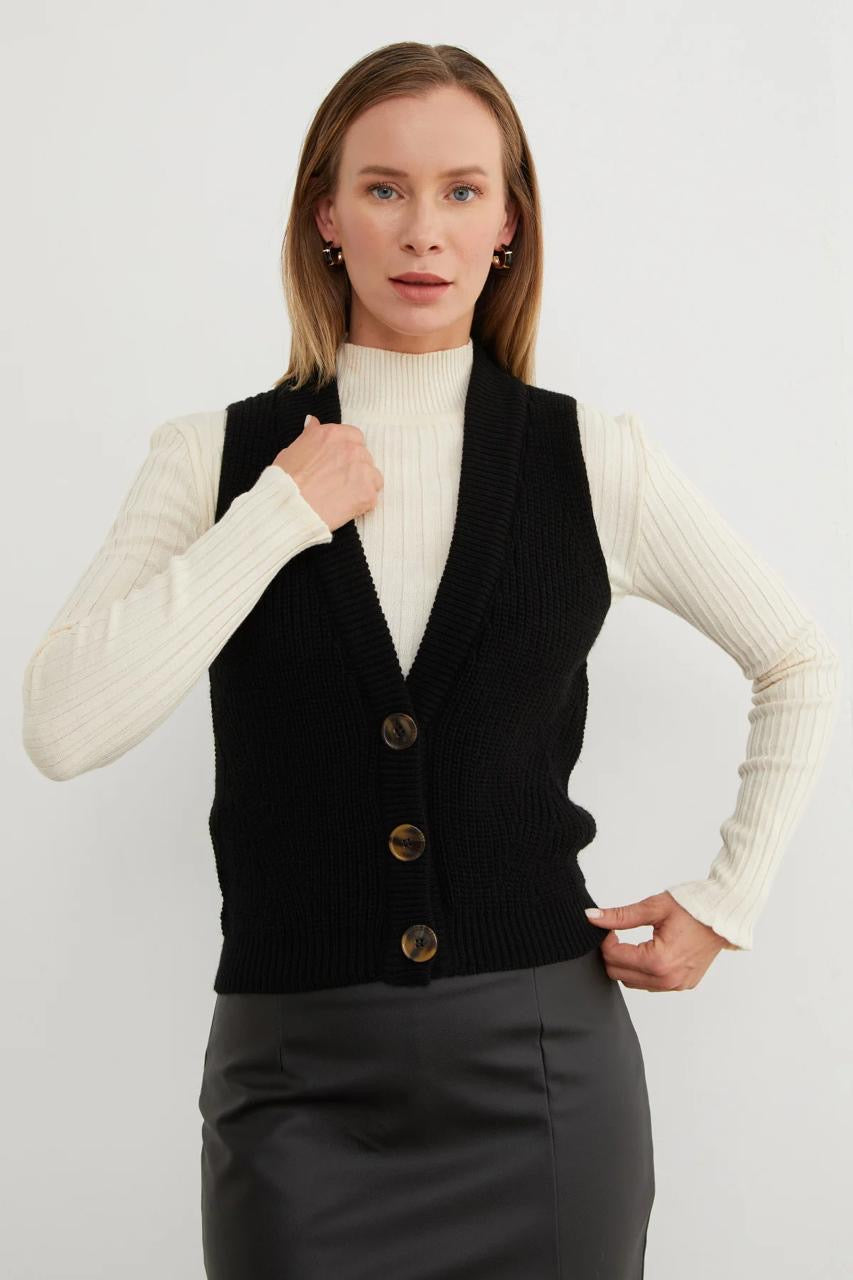 Black V-neck button-front knitted vest layered over a cream top